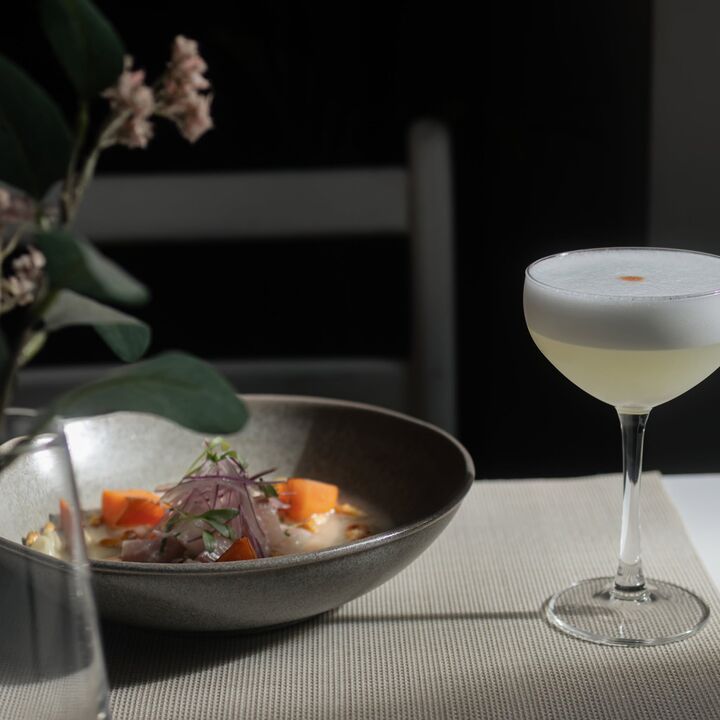 Um pisco sour num copo de pé ao lado de uma taça de ceviche.